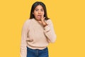 Young latin girl wearing wool winter sweater hand on mouth telling secret rumor, whispering malicious talk conversation Royalty Free Stock Photo