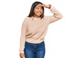 Young latin girl wearing wool winter sweater very happy and smiling looking far away with hand over head Royalty Free Stock Photo