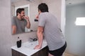 Young latin man brushing his teeth in front of the mirror in the bathroom at morning Royalty Free Stock Photo