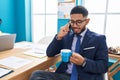Young latin man business worker talking on smartphone drinking coffee at office Royalty Free Stock Photo
