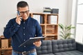 Young latin man business worker talking on smartphone reading document at office Royalty Free Stock Photo