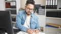 Young latin man business worker using computer taking notes at office Royalty Free Stock Photo