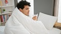 Young latin man covering with blanket holding thermometer at bedroom