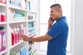 Young latin man customer smiling confident talking on smartphone at pharmacy