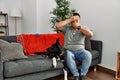 Young latin man and dog sitting on the sofa at home covering eyes and mouth with hands, surprised and shocked Royalty Free Stock Photo