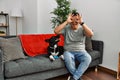 Young latin man and dog sitting on the sofa at home doing ok gesture like binoculars sticking tongue out, eyes looking through Royalty Free Stock Photo