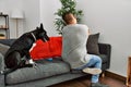 Young latin man and dog sitting on the sofa at home hugging oneself happy and positive from backwards Royalty Free Stock Photo