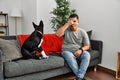 Young latin man and dog sitting on the sofa at home peeking in shock covering face and eyes with hand, looking through fingers Royalty Free Stock Photo
