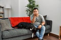Young latin man and dog sitting on the sofa at home smelling something stinky and disgusting, intolerable smell, holding breath Royalty Free Stock Photo