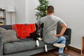 Young latin man and dog sitting on the sofa at home standing backwards looking away with arms on body Royalty Free Stock Photo