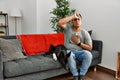 Young latin man and dog sitting on the sofa at home touching forehead for illness and fever, flu and cold, virus sick Royalty Free Stock Photo