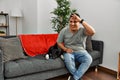 Young latin man and dog sitting on the sofa at home very happy and smiling looking far away with hand over head Royalty Free Stock Photo