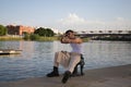 Young latin man dressed in beige pants, white t-shirt and black boots sitting on the mooring at the river pier in seville. The man Royalty Free Stock Photo