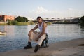 Young latin man dressed in beige pants, white t-shirt and black boots sitting on the mooring at the river pier in seville. The man Royalty Free Stock Photo