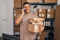 Young latin man ecommerce business worker talking on smartphone holding packages at office Royalty Free Stock Photo