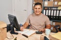 Young latin man ecommerce business worker using calculator writing on notebook at office Royalty Free Stock Photo