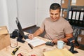 Young latin man ecommerce business worker using calculator writing on notebook at office Royalty Free Stock Photo