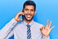 Young latin man having conversation talking on the smartphone doing ok sign with fingers, smiling friendly gesturing excellent Royalty Free Stock Photo