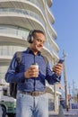 Young latin man with headphones looking at his mobile phone and holding a paper cup with coffee in his hand Royalty Free Stock Photo