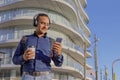Young latin man with headphones looking at his mobile phone and holding a paper cup with coffee in his hand Royalty Free Stock Photo