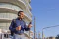 Young latin man with headphones looking at his mobile phone and holding a paper cup with coffee in his hand with copy space Royalty Free Stock Photo