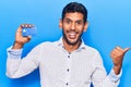 Young latin man holding credit card pointing thumb up to the side smiling happy with open mouth Royalty Free Stock Photo