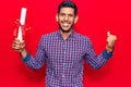 Young latin man holding graduate degree diploma screaming proud, celebrating victory and success very excited with raised arm Royalty Free Stock Photo