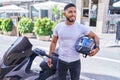 Young latin man holding helmet standing by motorbike at street Royalty Free Stock Photo