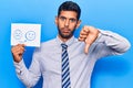 Young latin man holding sad to happy emotion paper with angry face, negative sign showing dislike with thumbs down, rejection Royalty Free Stock Photo