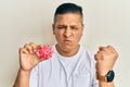 Young latin man holding virus toy annoyed and frustrated shouting with anger, yelling crazy with anger and hand raised Royalty Free Stock Photo