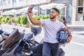 Young latin man make selfie by smartphone standing by motorbike at street Royalty Free Stock Photo