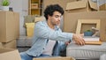 Young latin man packing cardboard box holding books at new home Royalty Free Stock Photo