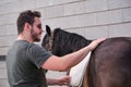 Young latin man putting on the saddle blanket to his horse and stroking it.