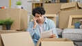 Young latin man reading document talking on smartphone looking upset at new home Royalty Free Stock Photo