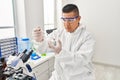 Young latin man scientist pouring liquid on cannabis herb sample at laboratory