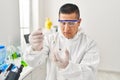 Young latin man scientist pouring liquid on cannabis herb sample at laboratory