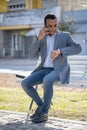 Young latin man sitting on a square bench talking on mobile phone and looking at his watch Royalty Free Stock Photo