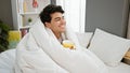 Young latin man smelling cup of coffee covering with blanket at bedroom