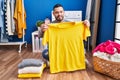 Young latin man smiling confident folding clothes at laundry room