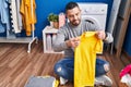 Young latin man smiling confident folding clothes at laundry room