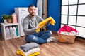 Young latin man smiling confident folding clothes at laundry room