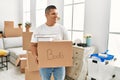 Young latin man smiling happy holding books cardboard box moving at new home Royalty Free Stock Photo