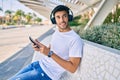 Young latin man smiling happy using smartphone and headphones sitting on the bench Royalty Free Stock Photo