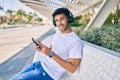 Young latin man smiling happy using smartphone and headphones sitting on the bench Royalty Free Stock Photo