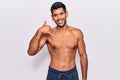 Young latin man standing shirtless smiling doing phone gesture with hand and fingers like talking on the telephone Royalty Free Stock Photo