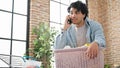 Young latin man talking on smartphone hanging clothes on clothesline at laundry room