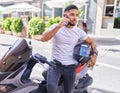 Young latin man talking on smartphone standing by motorbike at street Royalty Free Stock Photo