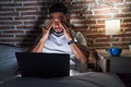 Young latin man tired using laptop sitting on bed at bedroom