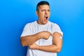 Young latin man using glucose meter button on arm angry and mad screaming frustrated and furious, shouting with anger