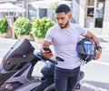 Young latin man using smartphone standing by motorbike at street Royalty Free Stock Photo